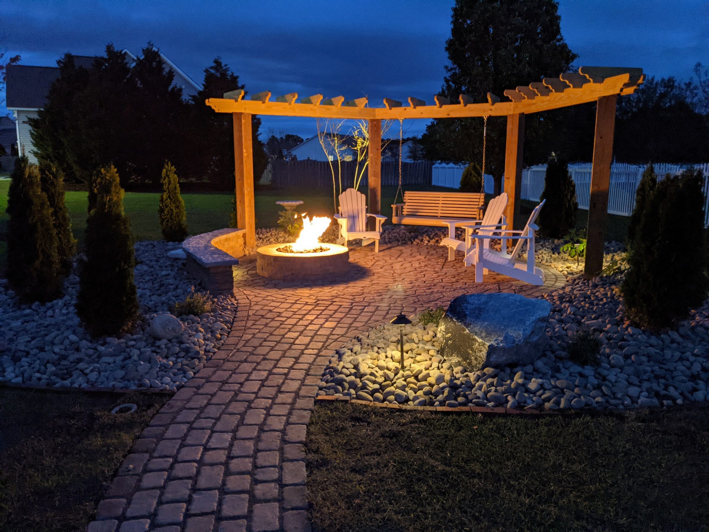 Outdoor fire pit with seating under pergola at night.