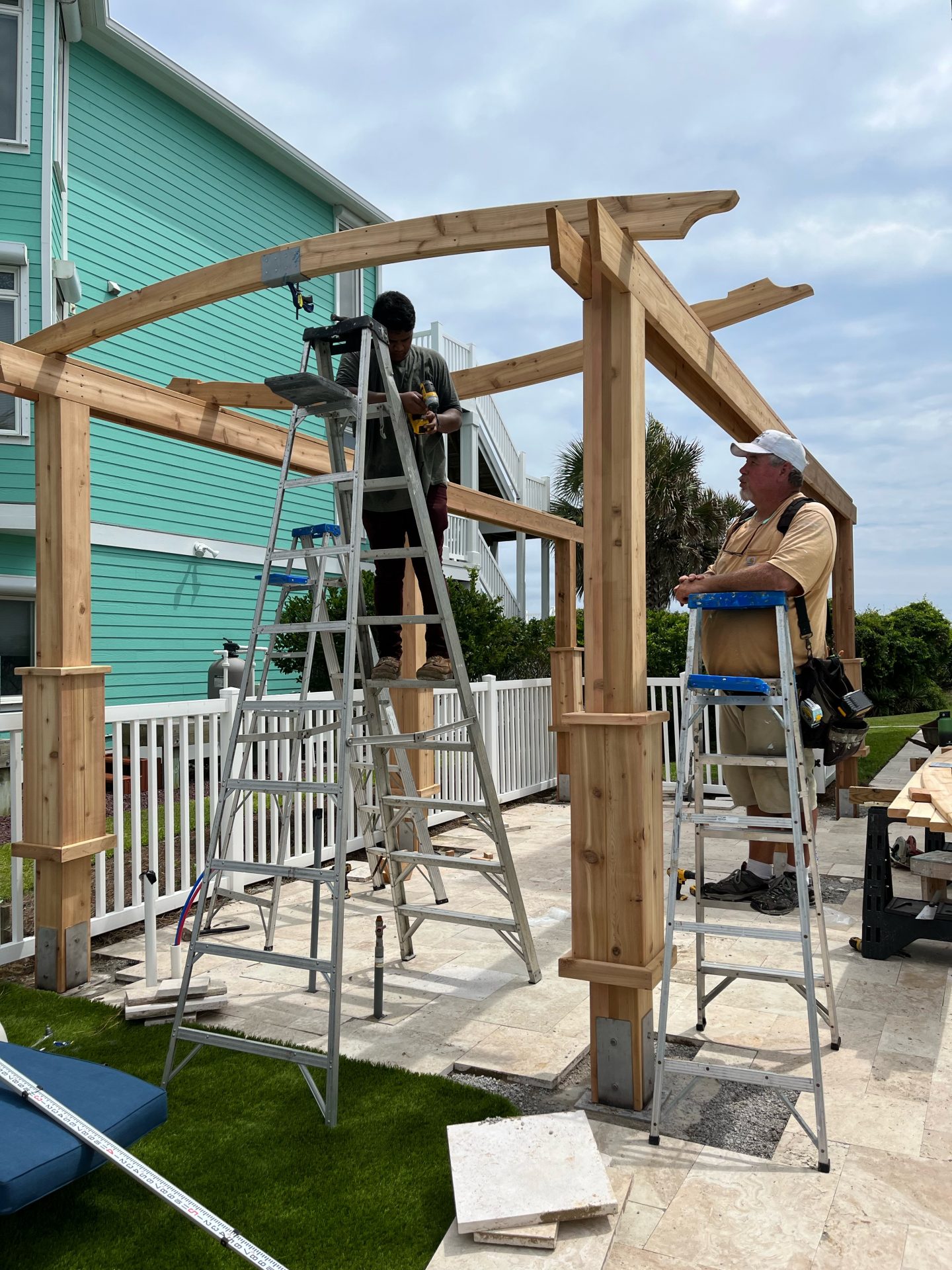Two workers constructing a wooden pergola structure.