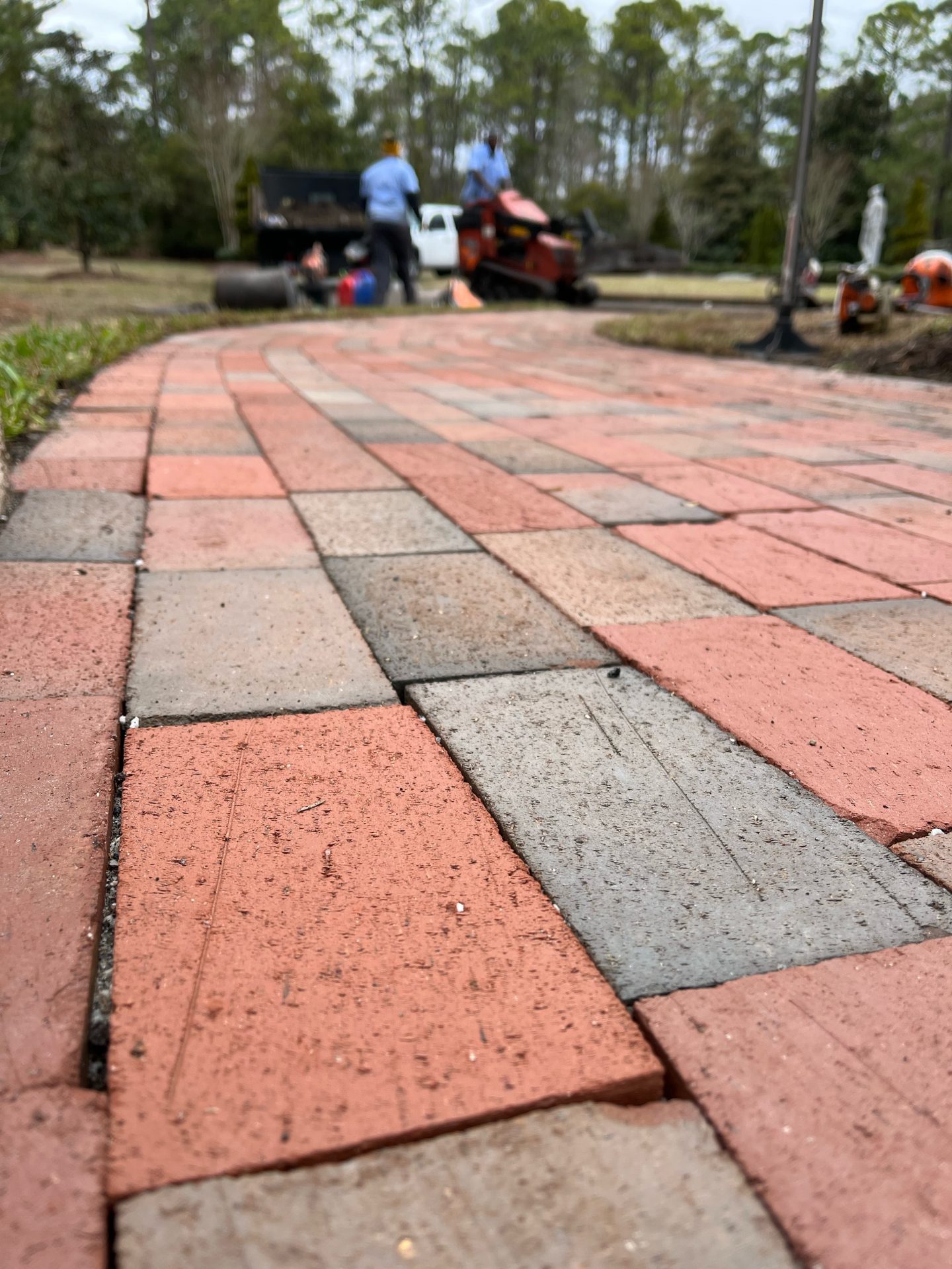 Brick paved path with people working in background.