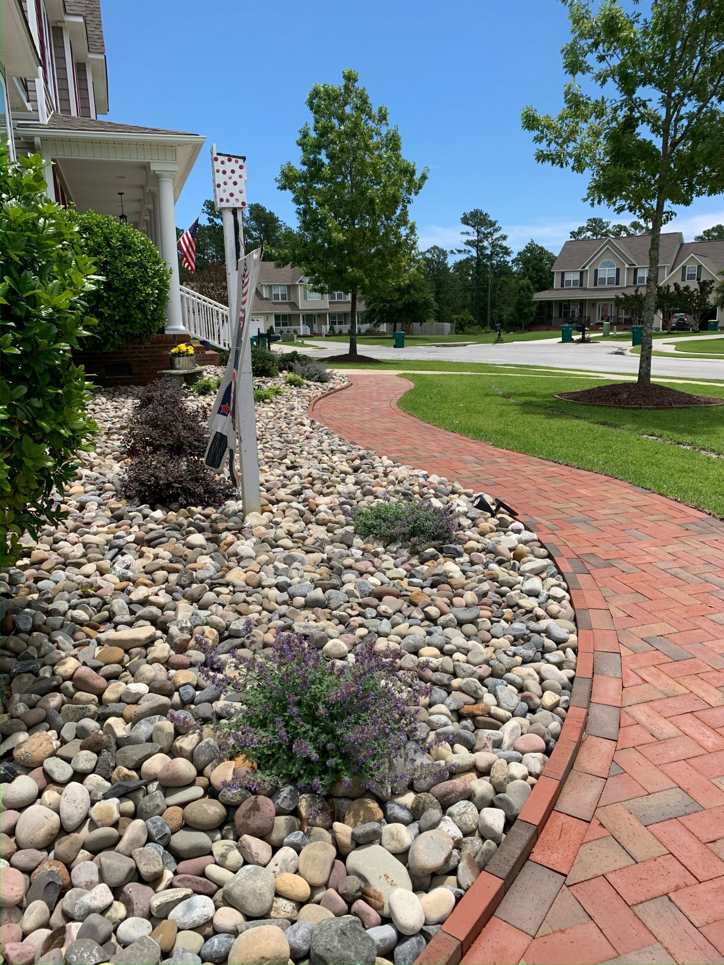 Brick walkway beside landscaped front yard with stones.