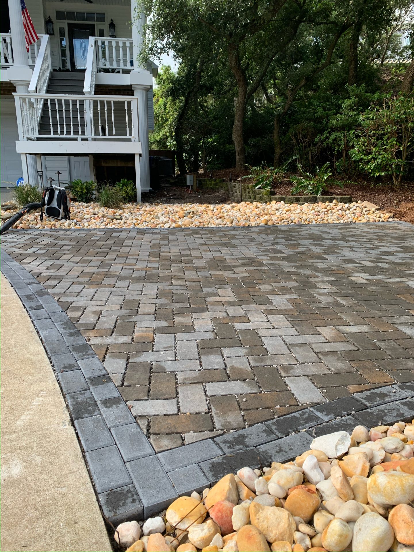 Paved driveway with stone border near forested house.
