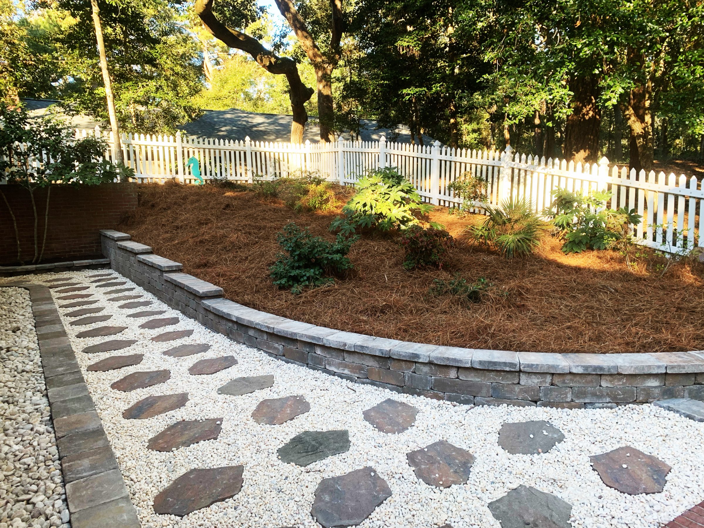 Stone path in landscaped garden with white fence.