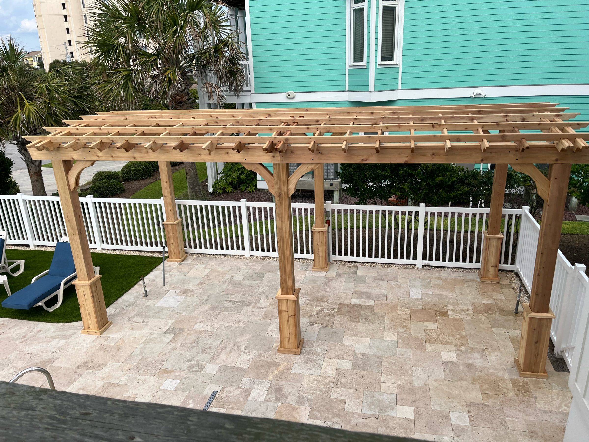 Wooden pergola on a patio with white fence.