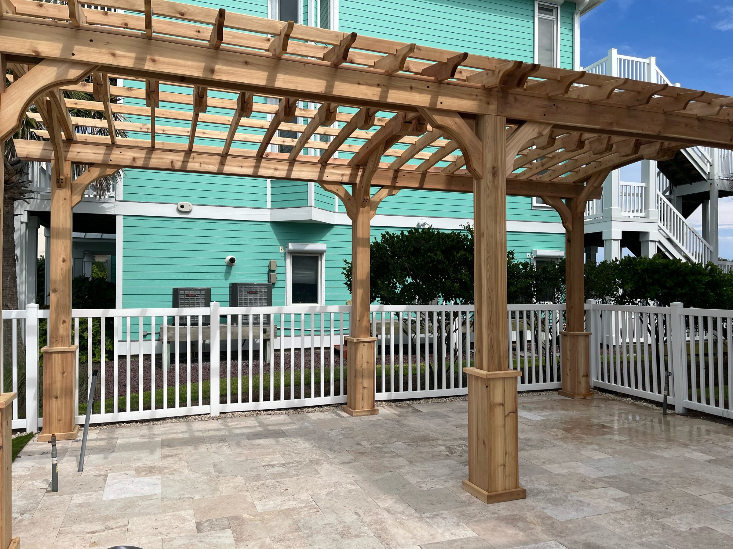 Wooden pergola on patio with turquoise house background.