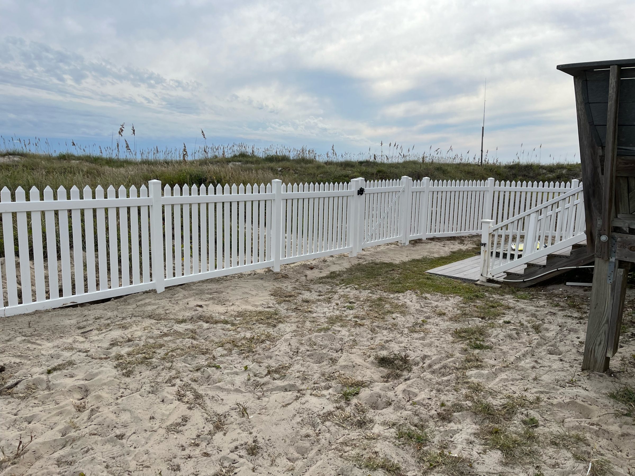 White picket fence on sandy beach path.