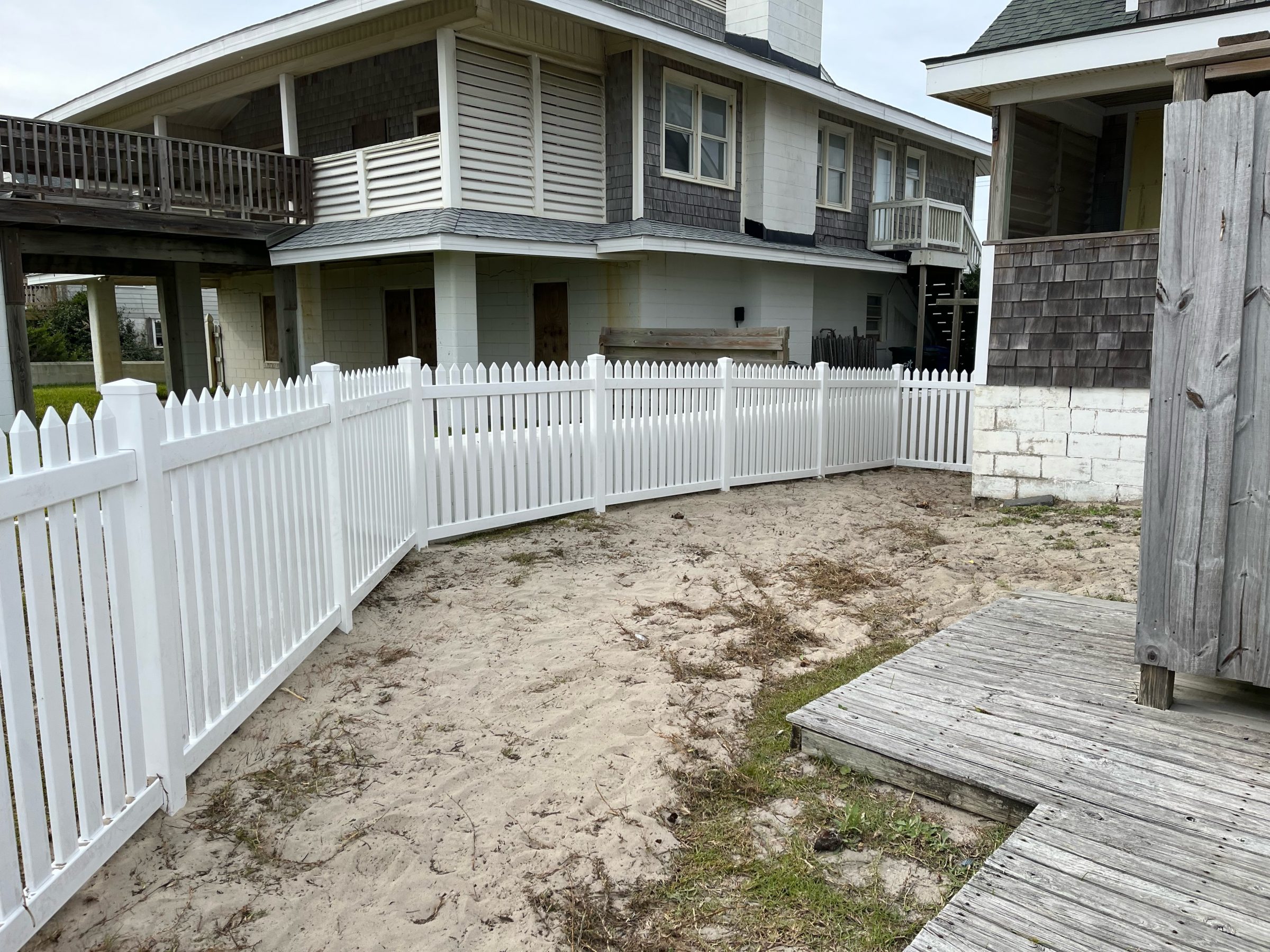 White picket fence around sandy backyard area.