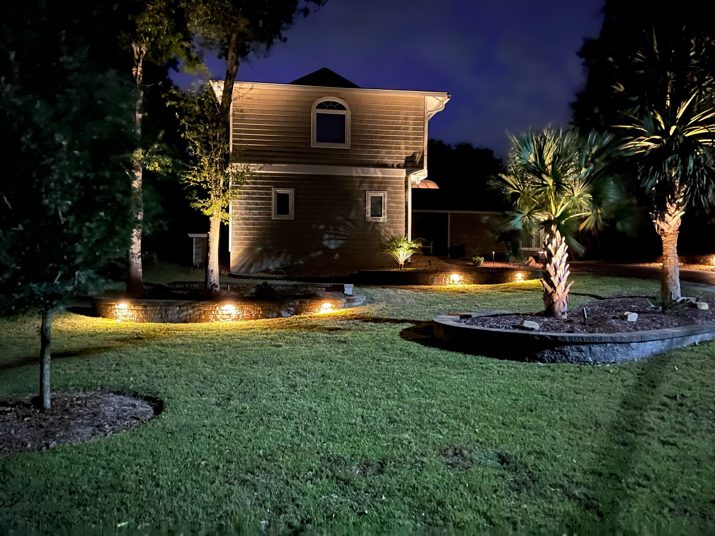 House with illuminated landscape and trees at night.