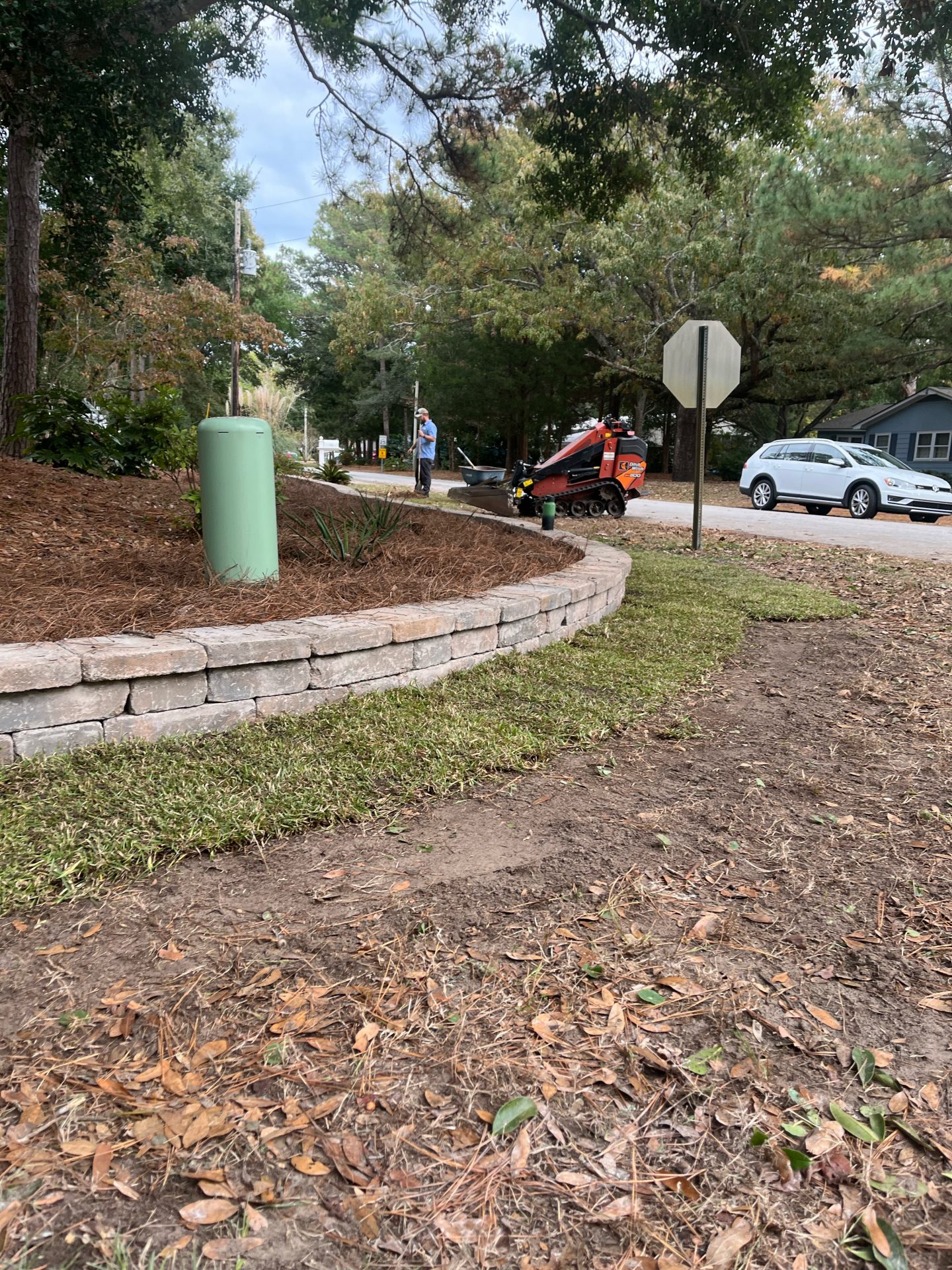 Worker operating mini loader on landscaped street corner.