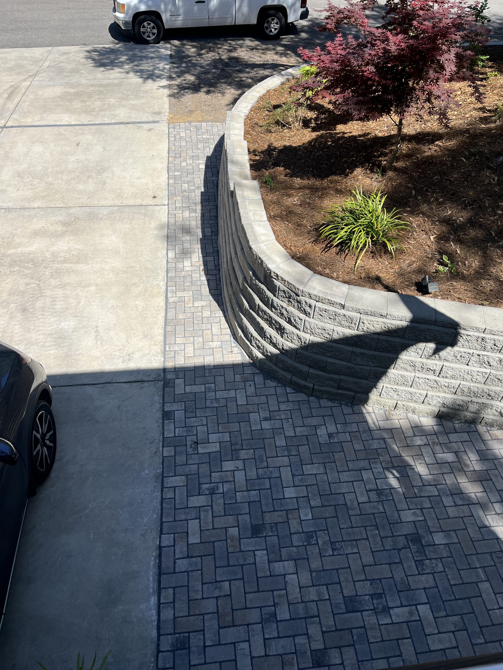 Paved driveway with car and brick wall garden.
