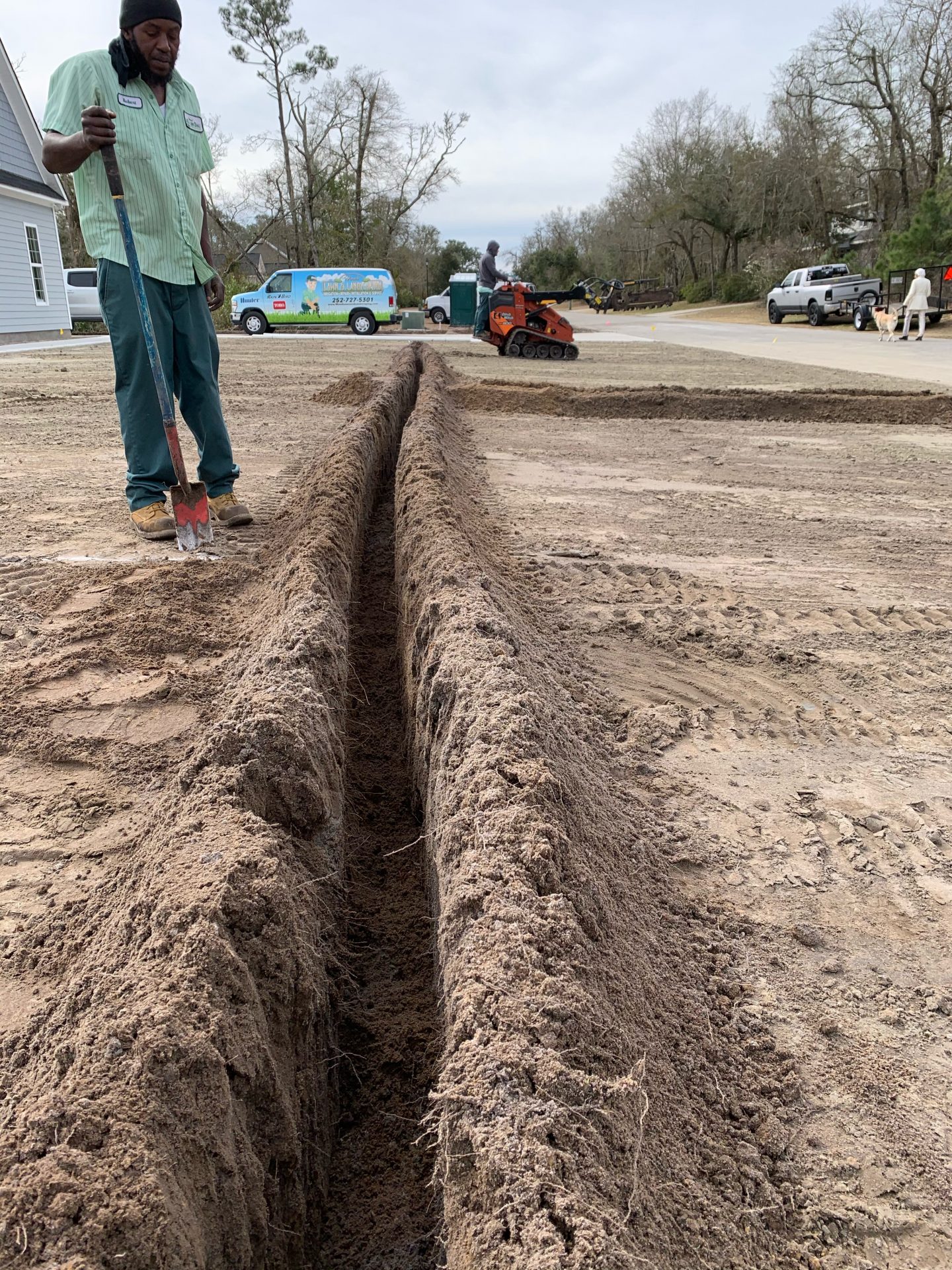 Construction worker standing by dug trench.