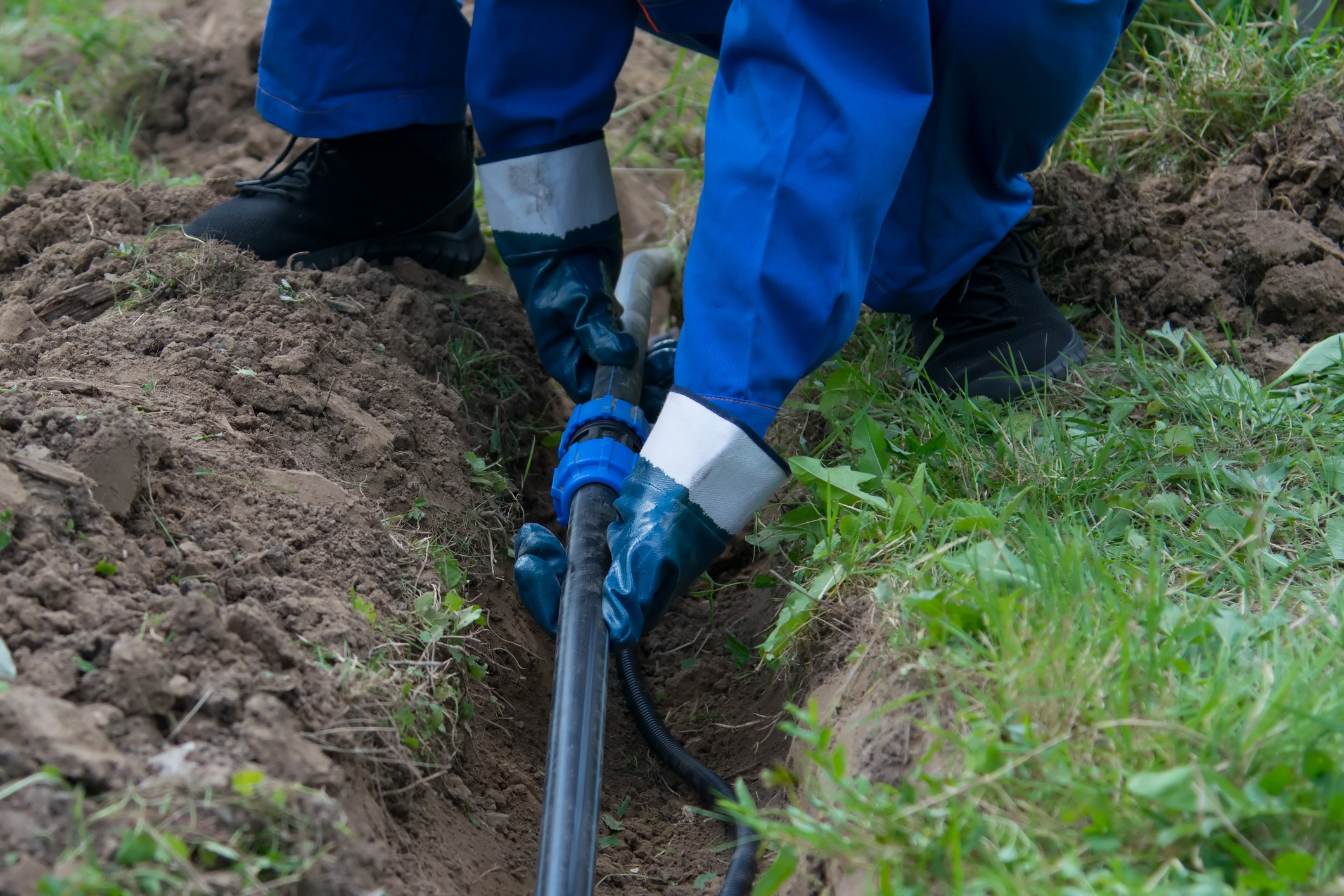Worker installing pipe in trench outdoors